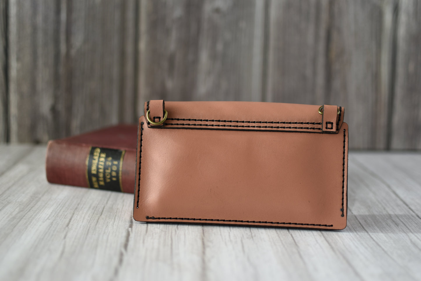 Brown leather cell phone purse on a wooden surface with a book in the background