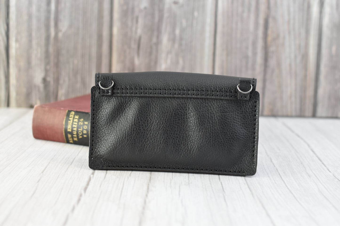 Black leather cell phone purse on a wooden surface with a book in the background