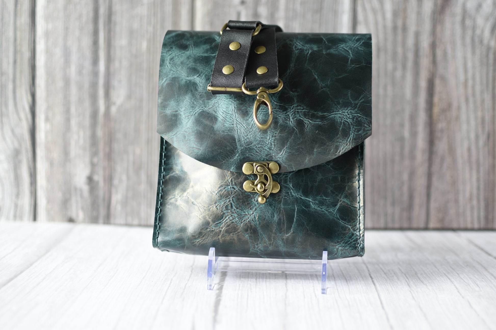 Green marbled purse with a gold clasp on a white background with a black strap.