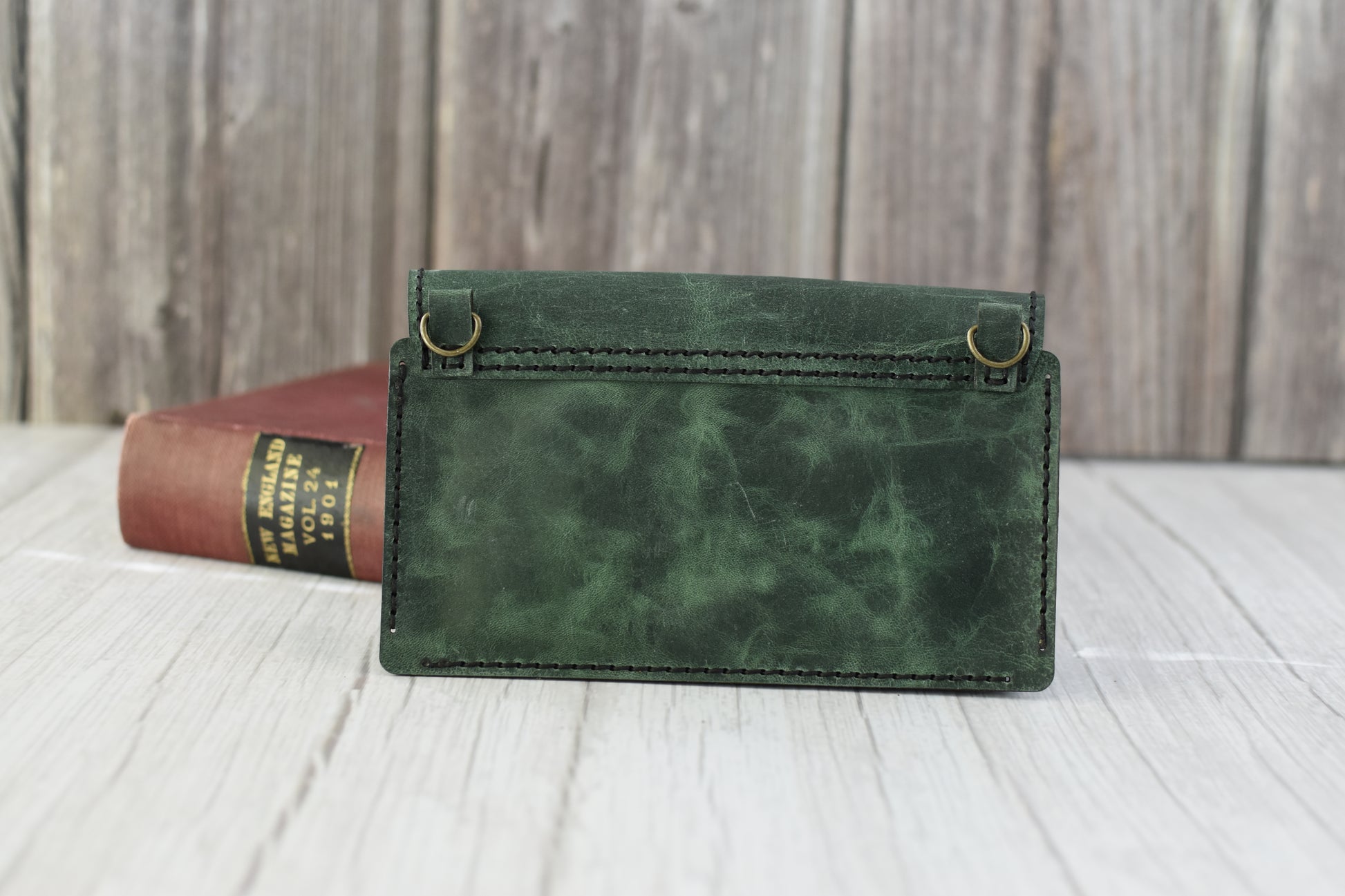 Green marbled leather cell phone purse on a wooden surface with a book in the background