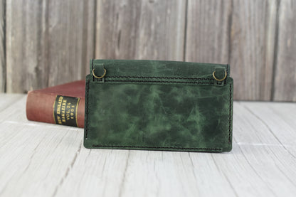 Green marbled leather cell phone purse on a wooden surface with a book in the background